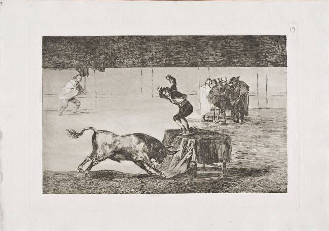 A black and white print of a man in an arena, standing on a table with arms raised and feet in a vice, facing a charging bull, with figures nearby